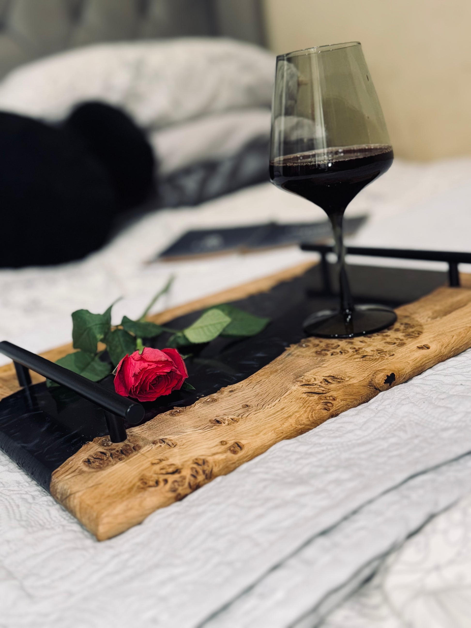 Oak burr and black onyx epoxy serving tray staged with a glass of wine and a rose on a bed with an open book
